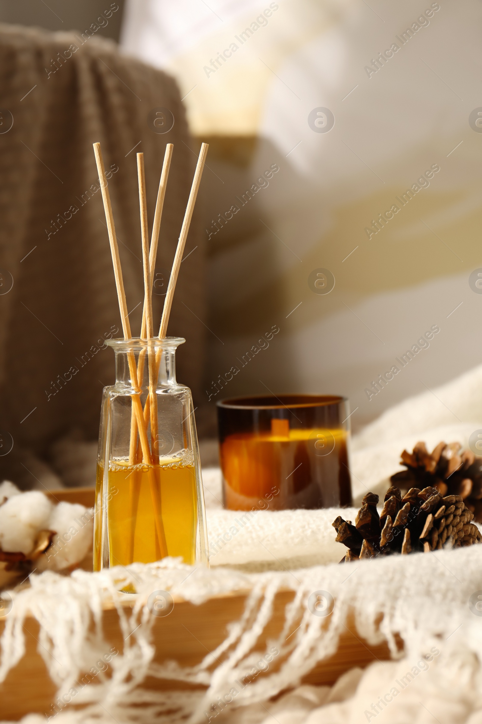 Photo of Reed air freshener, candle and pine cones on wooden tray indoors