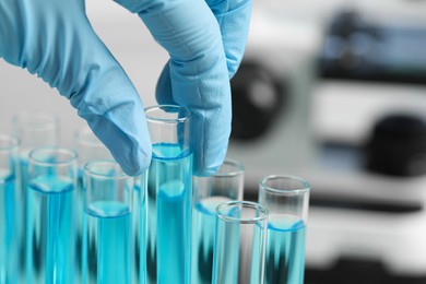 Scientist taking test tube with light blue liquid in laboratory, closeup