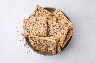 Photo of Cereal crackers with flax, sunflower and sesame seeds in bowl on light textured table, top view