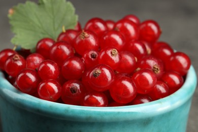 Many ripe red currants and leaf in bowl on blurred background, closeup