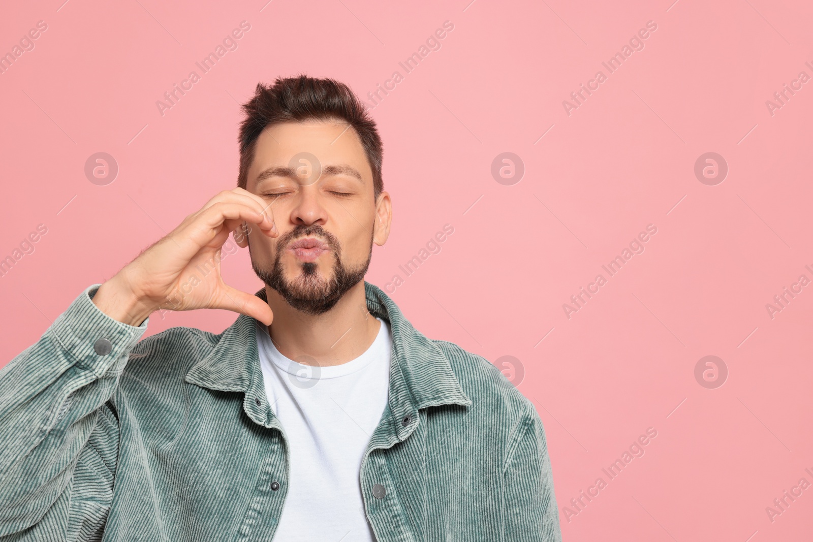 Photo of Handsome man blowing kiss on pink background. Space for text