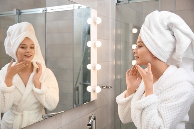 Photo of Beautiful woman with towel on head near mirror in bathroom