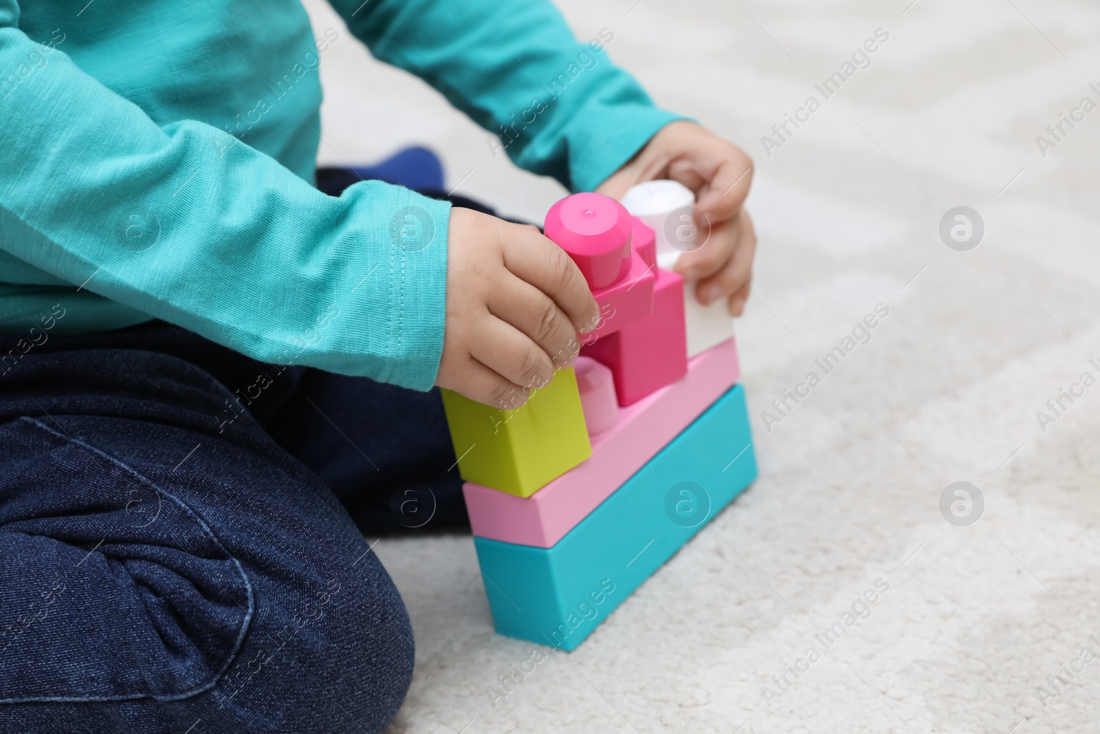 Photo of Little child playing with building blocks on carpet, closeup