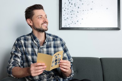 Happy man holding greeting card on sofa in living room