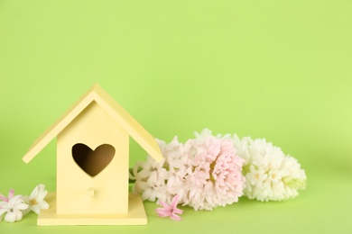 Photo of Stylish bird house and fresh hyacinths on green background. Space for text