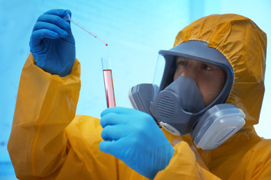 Photo of Scientist in chemical protective suit dripping reagent  into test tube at laboratory. Virus research