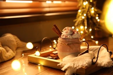 Photo of Tasty hot drink with whipped cream and Christmas lights on wooden table