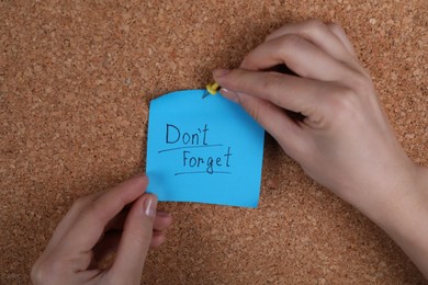 Photo of Woman pinning paper note with phrase Don't Forget to cork board, closeup
