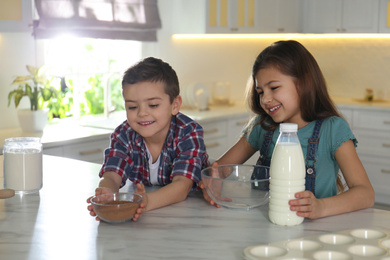 Photo of Cute little children at table with cooking ingredients in kitchen
