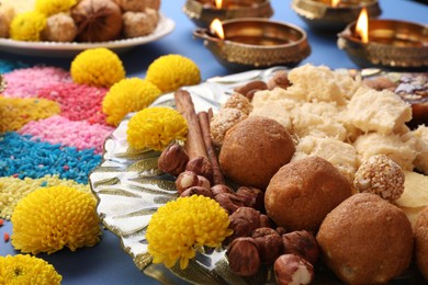 Photo of Diwali celebration. Tasty Indian sweets, colorful rangoli and diya lamps on blue table, closeup