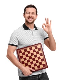 Smiling man holding chessboard and showing OK gesture on white background