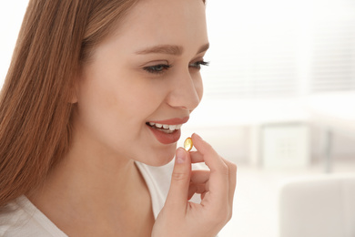 Photo of Young woman taking vitamin capsule on light background