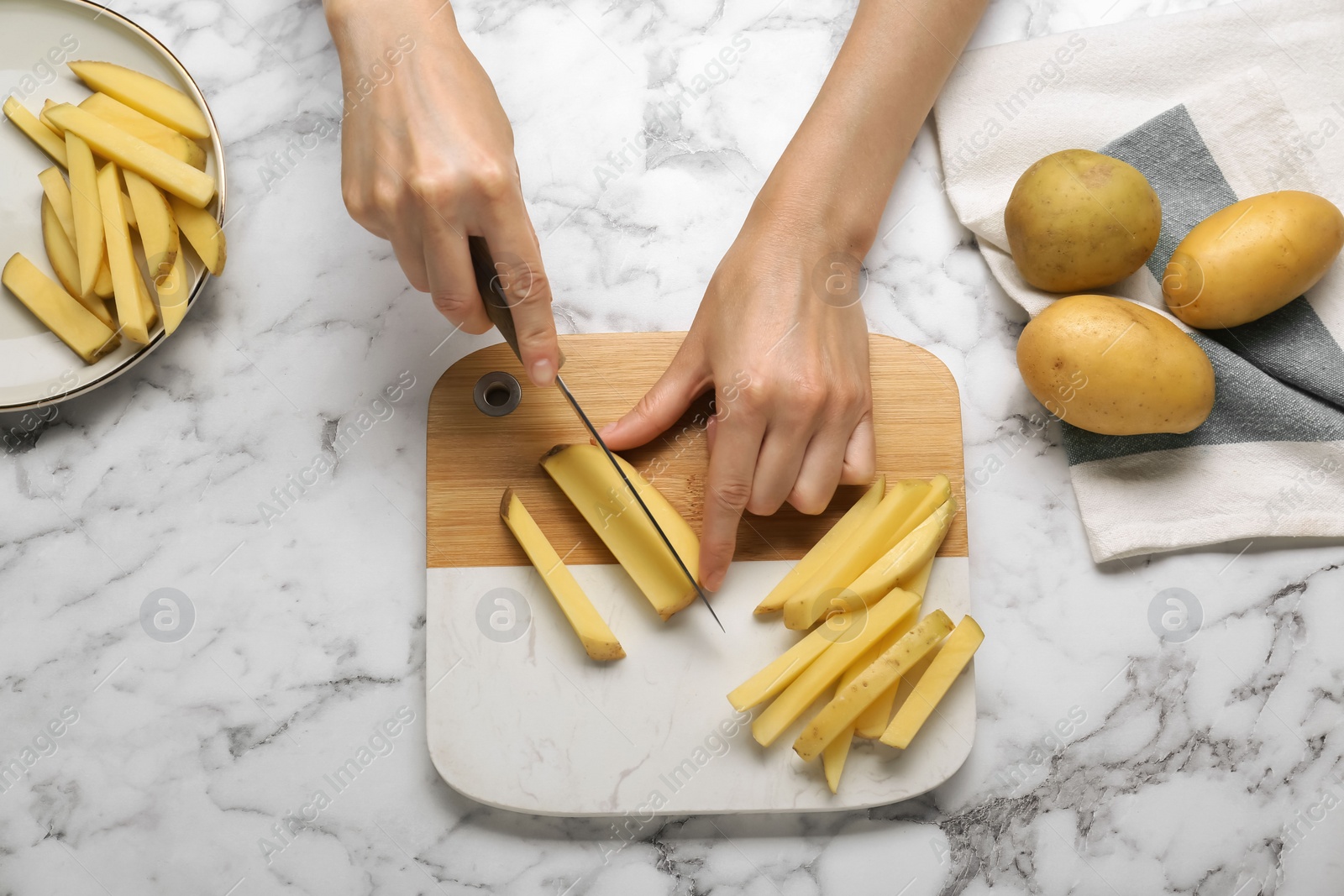 Photo of Woman cutting potato at white marble table, top view. Cooking delicious French fries