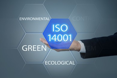 Image of Businessman holding virtual icon with text ISO 14001 on grey background, closeup