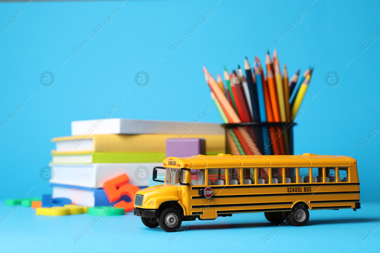 Photo of School bus model, books and color pencils on light blue background. Transport for students