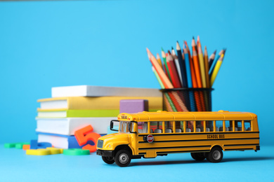 Photo of School bus model, books and color pencils on light blue background. Transport for students
