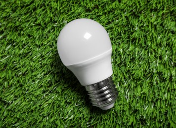Photo of New light bulb on fresh green grass, top view