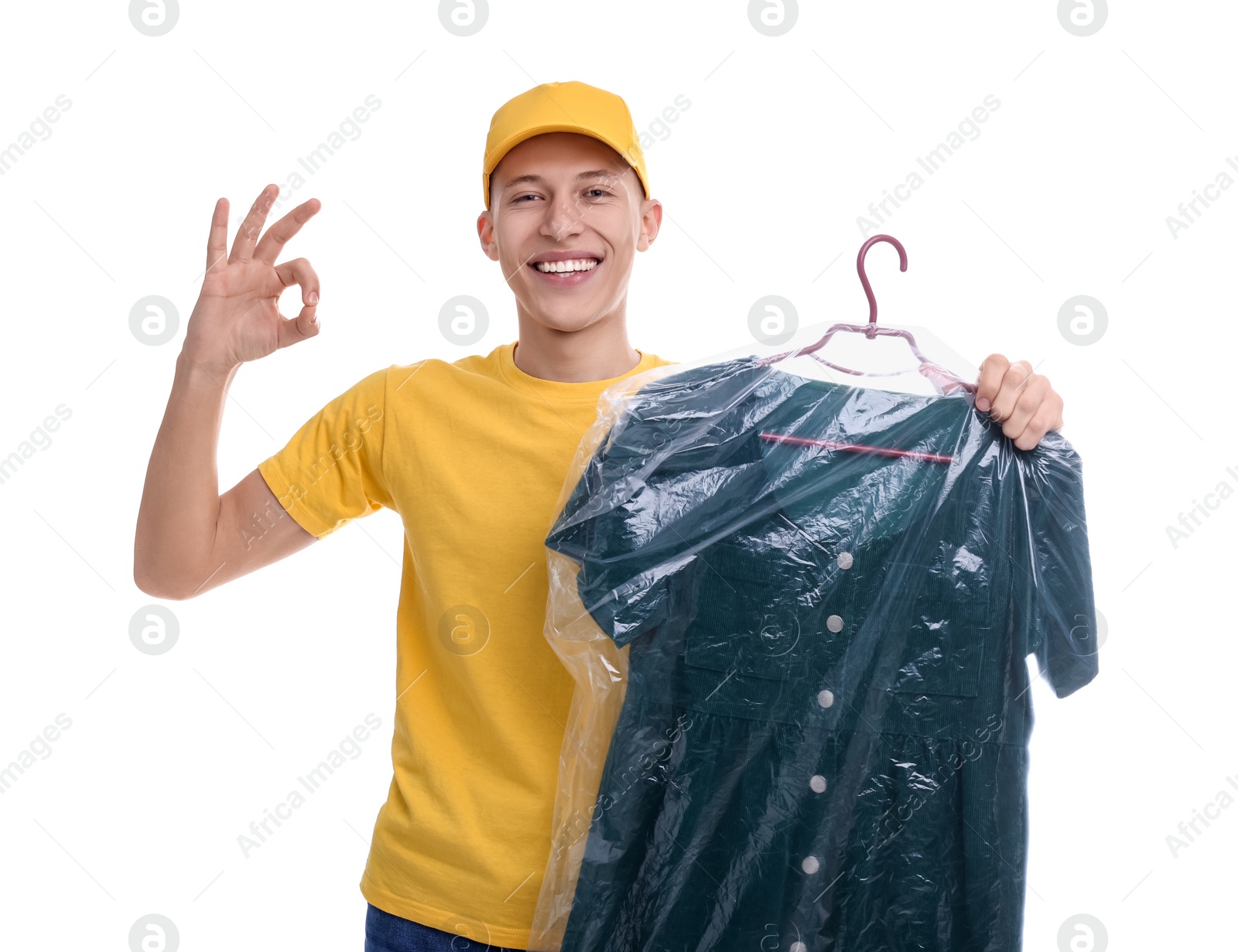 Photo of Dry-cleaning delivery. Happy courier holding dress in plastic bag and showing OK gesture on white background