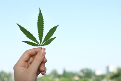 Photo of Woman holding hemp leaf against blue sky, closeup. Space for text