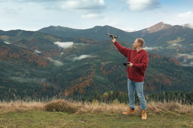 Young man with modern drone in mountains, space for text