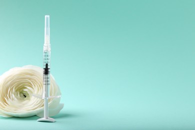 Photo of Cosmetology. Medical syringe and ranunculus flower on turquoise background, space for text