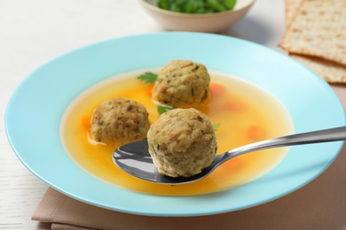 Photo of Spoon with matzoh ball over dish of soup on table, closeup. Jewish cuisine