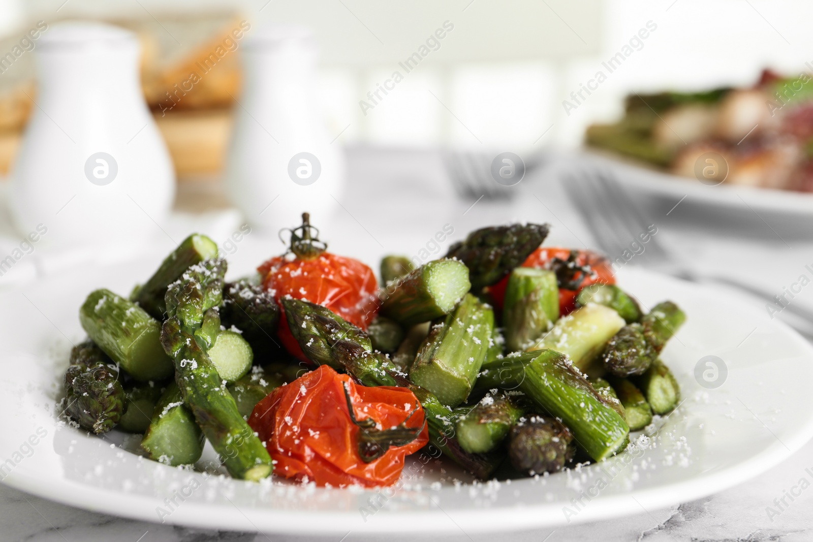 Photo of Oven baked asparagus with cherry tomatoes on white plate, closeup