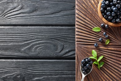 Tasty fresh bilberries and green leaves on black wooden table, top view. Space for text