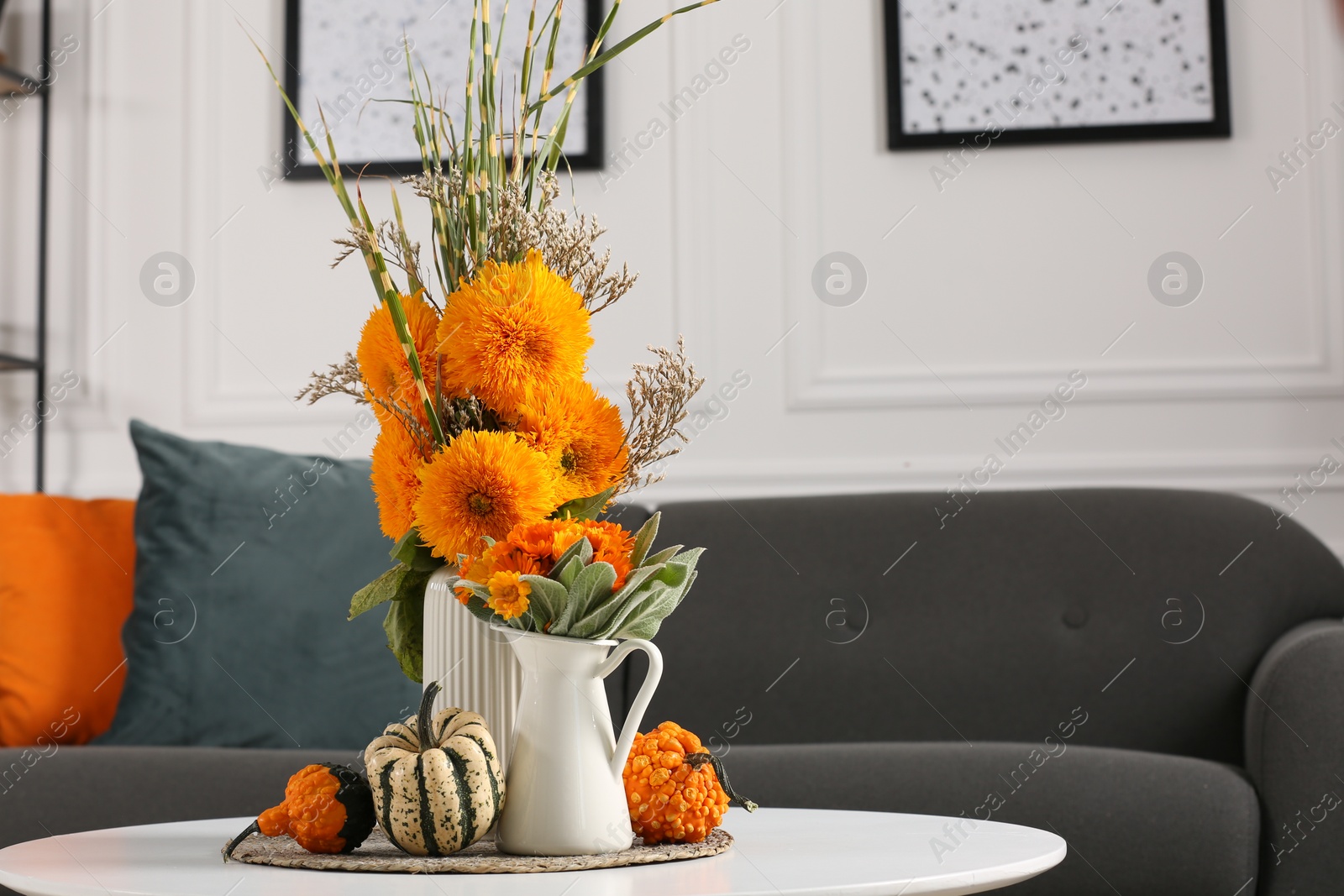 Photo of Beautiful autumn bouquets and pumpkins on coffee table near sofa in room