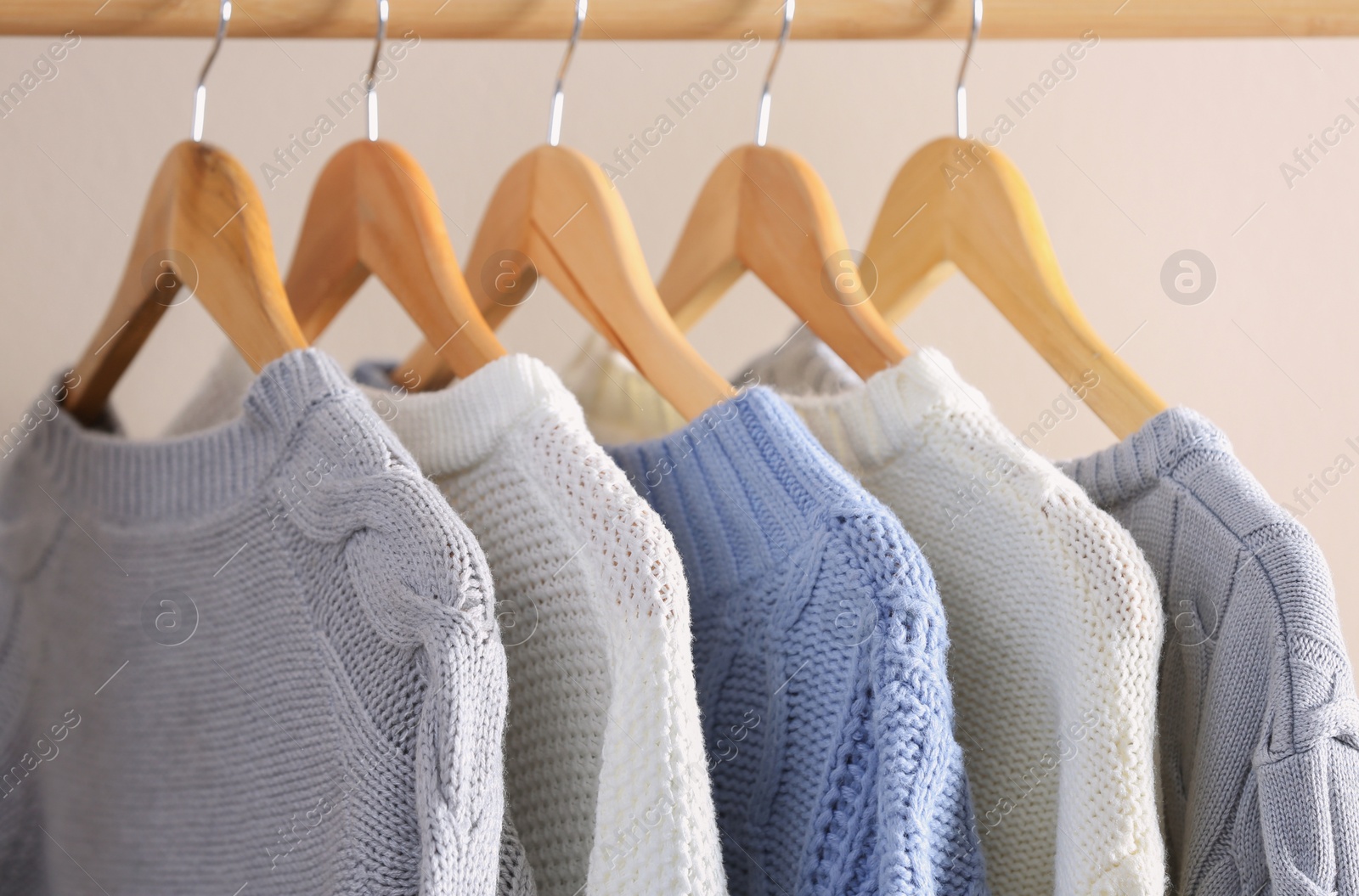 Photo of Collection of warm sweaters hanging on rack near light wall, closeup