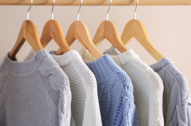 Collection of warm sweaters hanging on rack near light wall, closeup