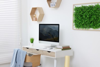 Green artificial plant wall panel and desk with computer in light room. Interior design