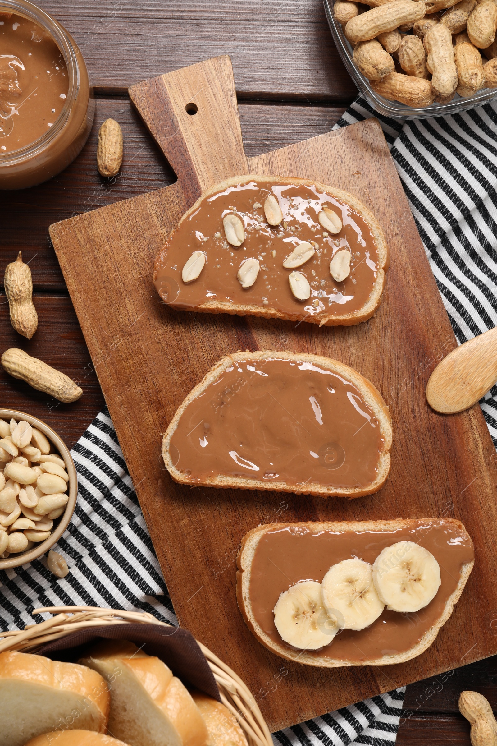 Photo of Toasts with tasty nut butter, banana slices and peanuts on wooden table, flat lay