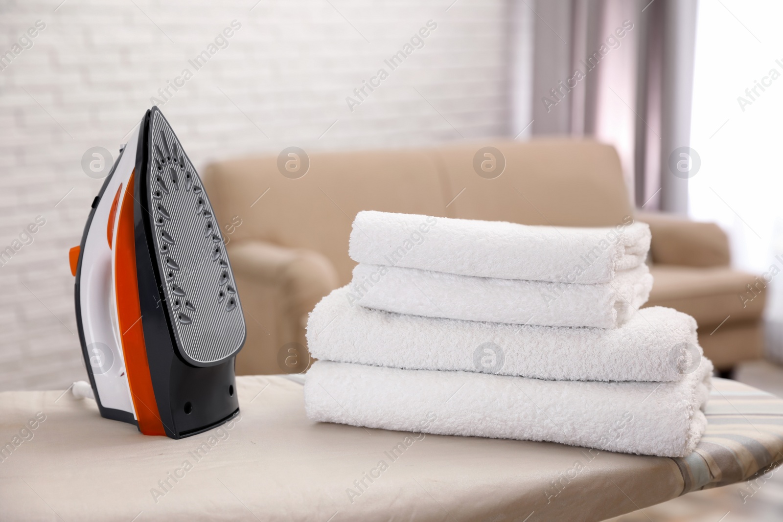 Photo of New modern iron and clean towels on board indoors. Laundry day