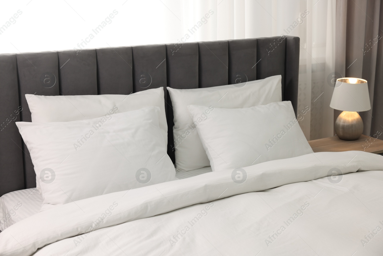 Photo of Soft white pillows and duvet on bed at home