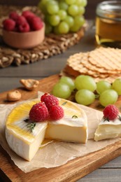 Photo of Brie cheese served with berries and honey on wooden table, closeup