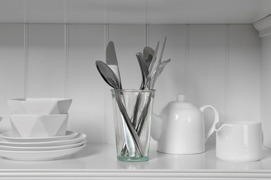 Photo of White shelving unit with dishware and cutlery