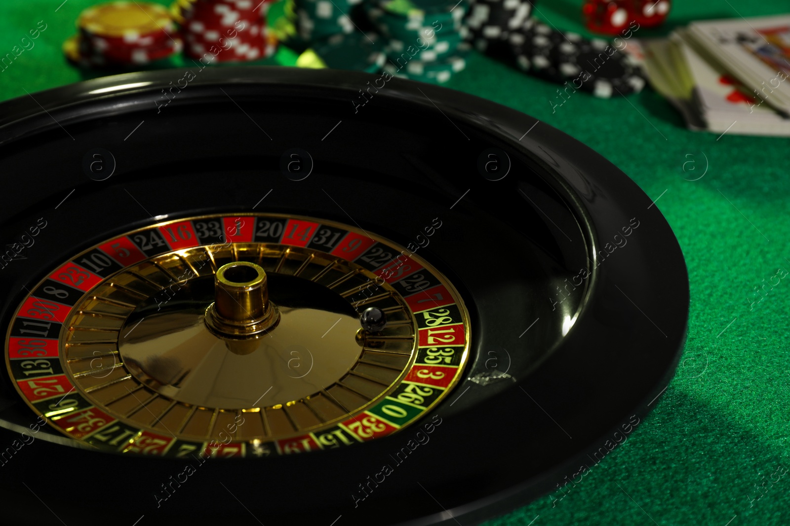 Photo of Roulette wheel with ball, playing cards and chips on green table, closeup. Casino game