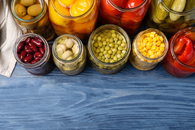 Photo of Glass jars with different pickled vegetables on blue wooden table, flat lay. Space for text