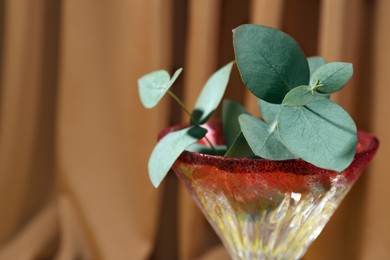 Photo of Beautiful martini glass with eucalyptus leaves against brown background, closeup. Space for text