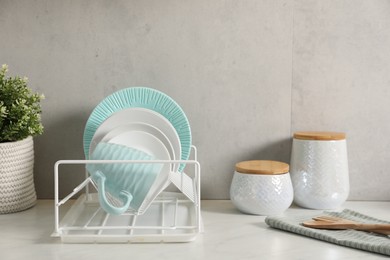 Drainer with different clean dishware and cup on light table indoors