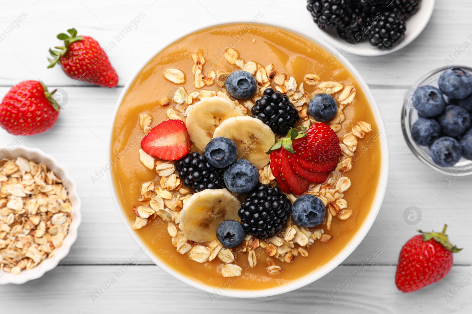 Photo of Delicious smoothie bowl with fresh berries, banana and oatmeal on white wooden table, flat lay