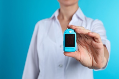 Female doctor holding pulsimeter on color background, closeup. Medical object