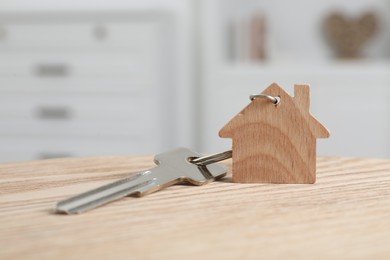 Photo of Key with keychain in shape of house on wooden table indoors, closeup. Space for text