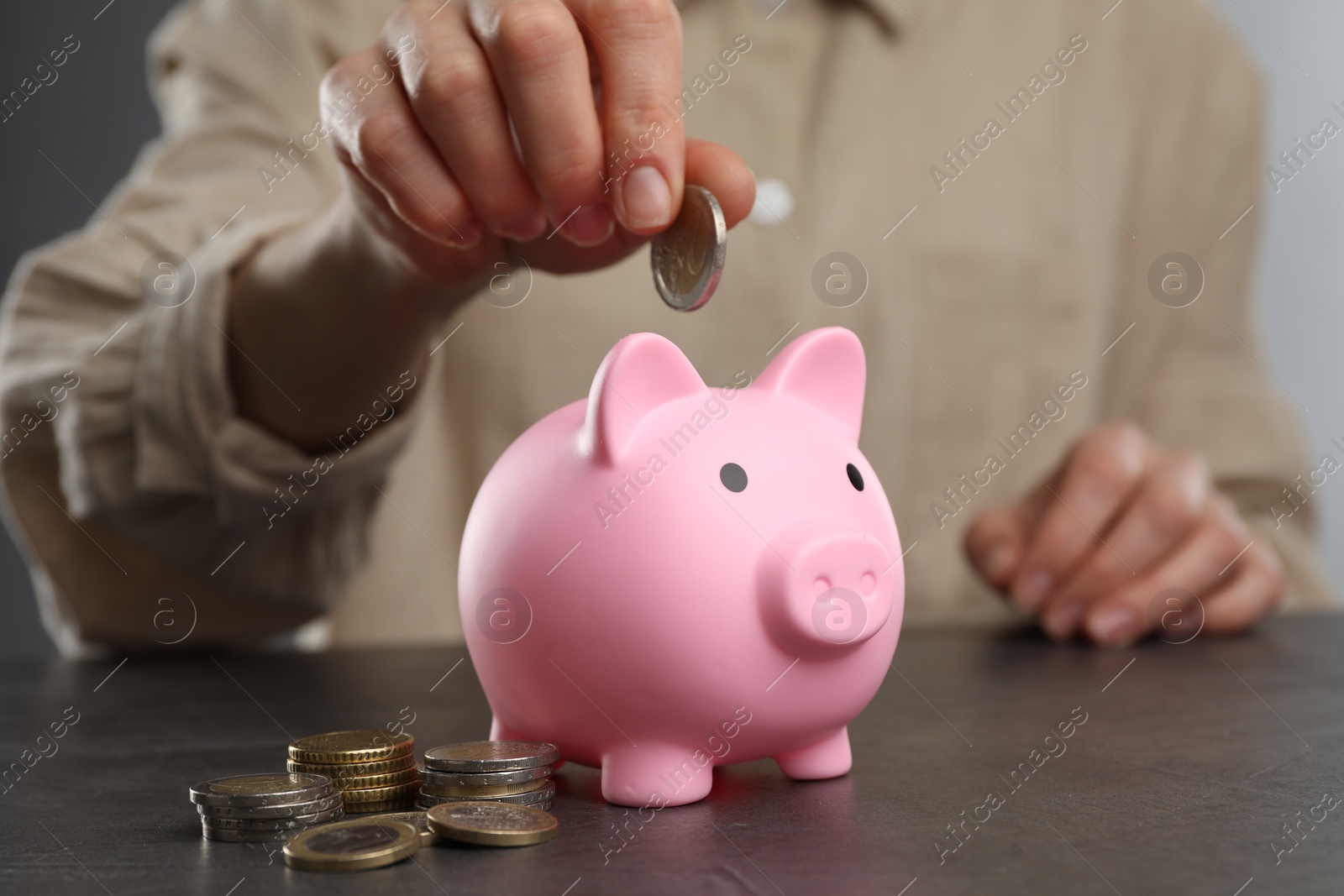 Photo of Woman putting coin into pink piggy bank at black table, closeup