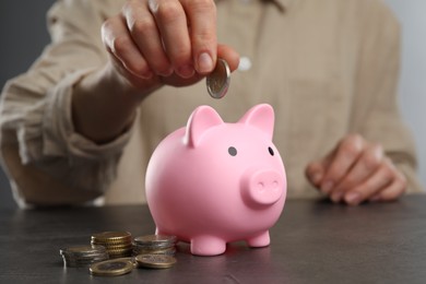 Photo of Woman putting coin into pink piggy bank at black table, closeup