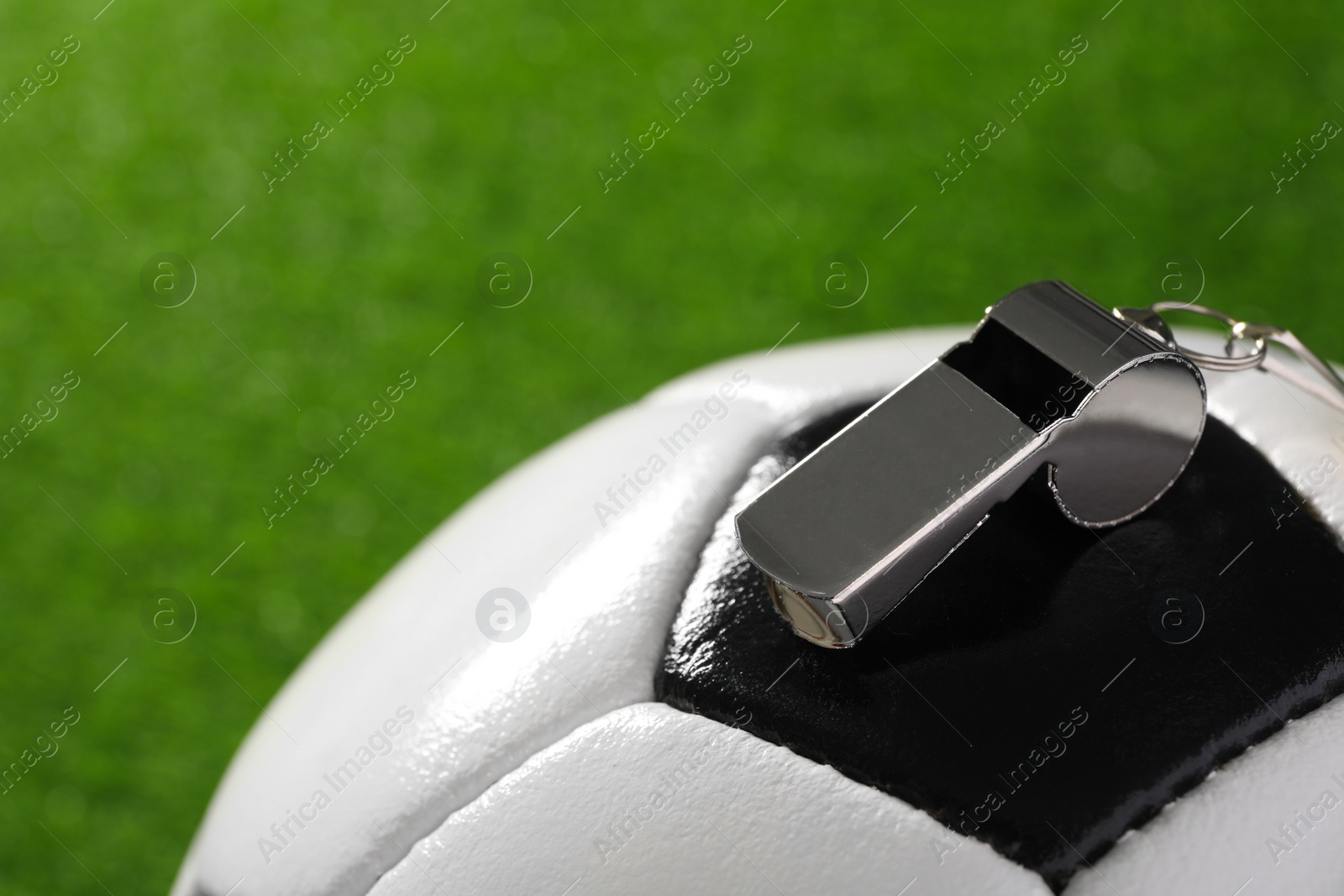 Photo of Football referee equipment. Soccer ball and metal whistle on green grass, closeup with space for text