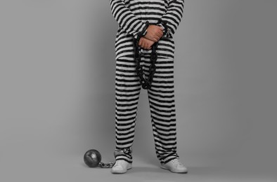 Photo of Prisoner in special uniform with chained hands and metal ball on grey background, closeup