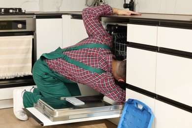 Photo of Serviceman repairing and examining dishwasher in kitchen