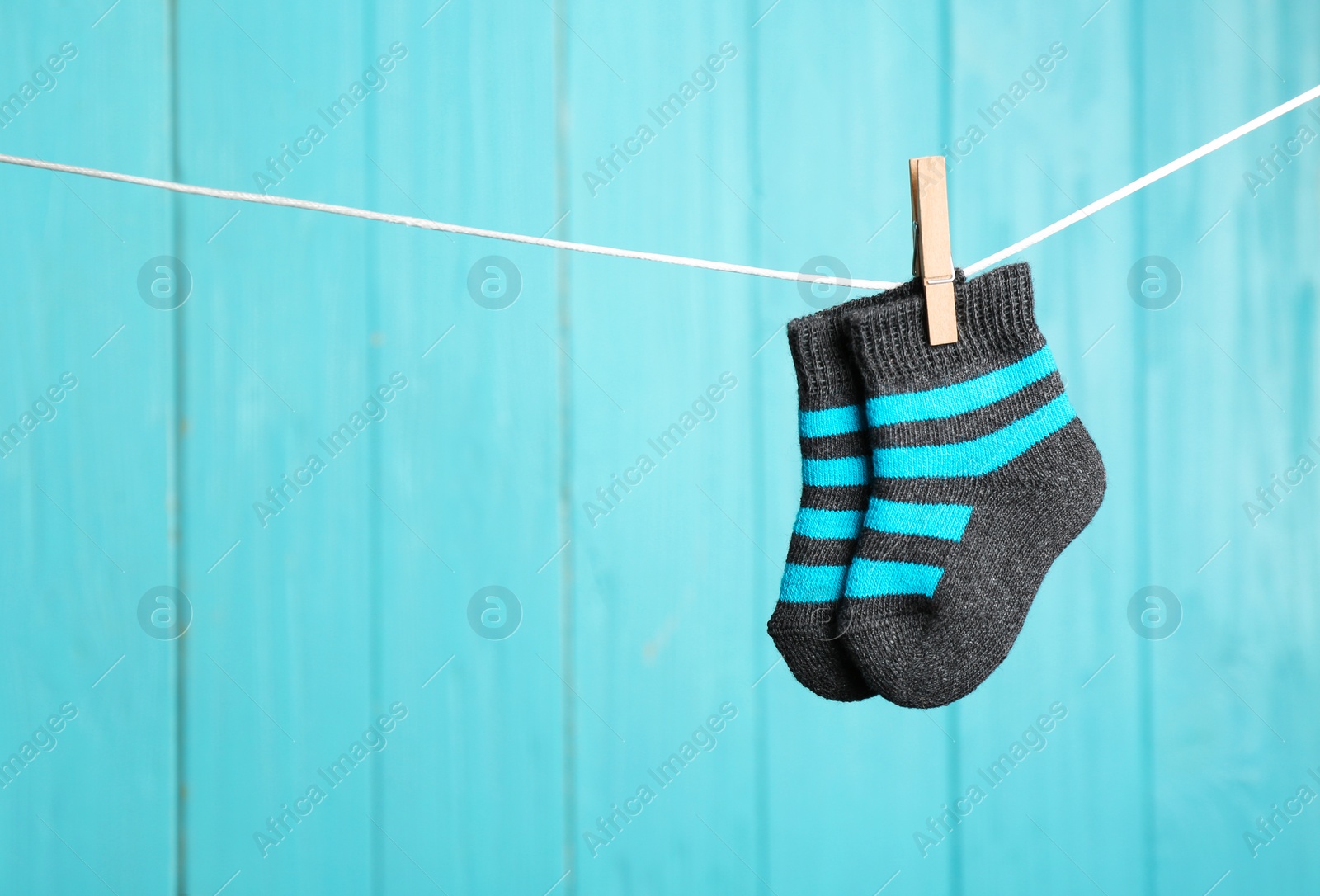 Photo of Baby socks on laundry line against color wooden background, space for text. Child accessories